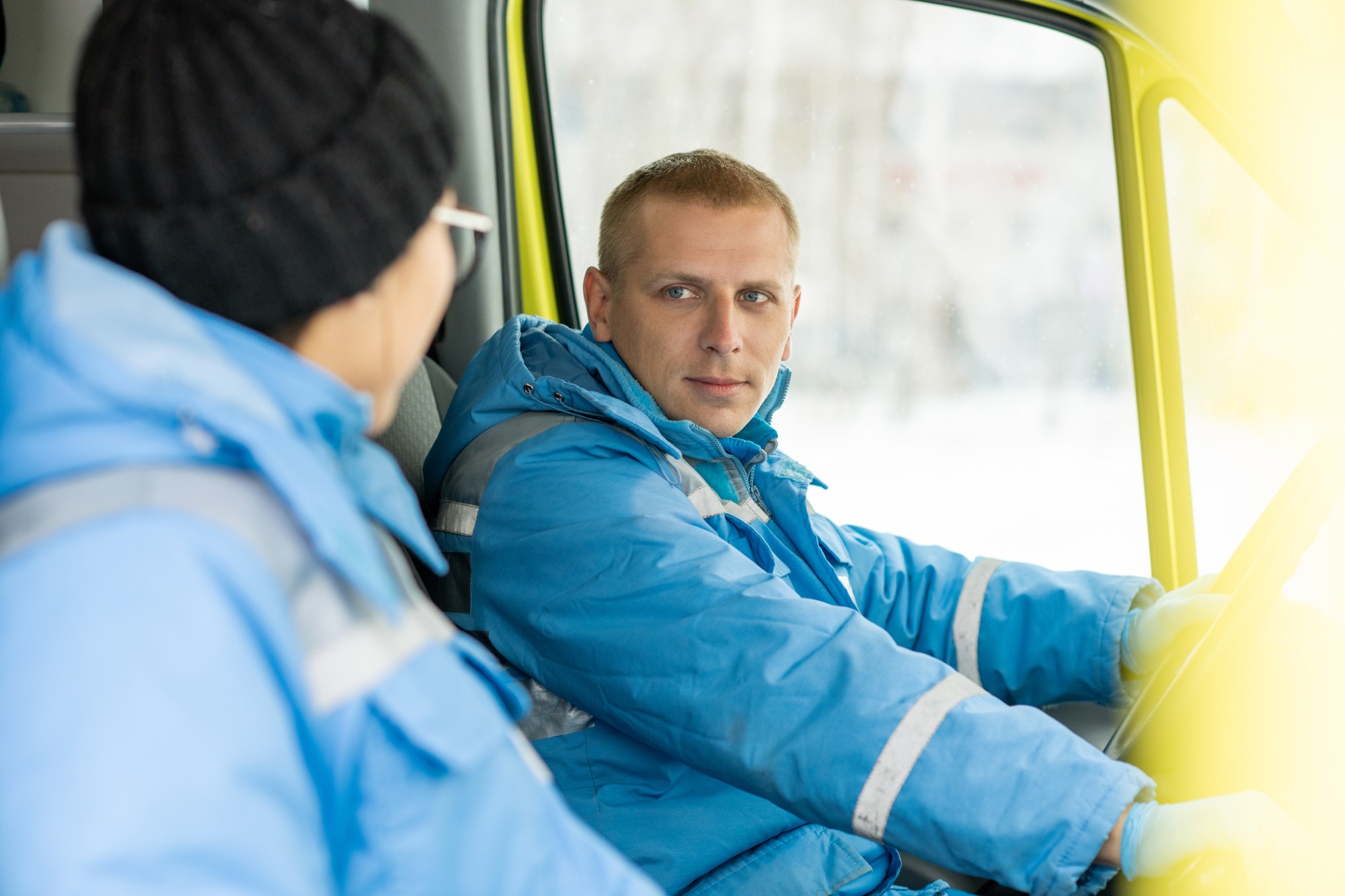 Young driver of ambulance car talking to female paramedic and steering